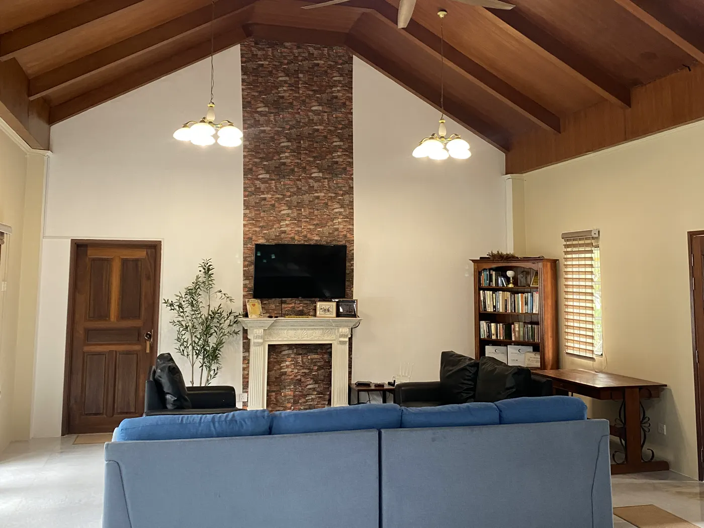 The Tudor Bungalow's lounge with a vaulted timber ceiling, brick fireplace wall and blue sofas