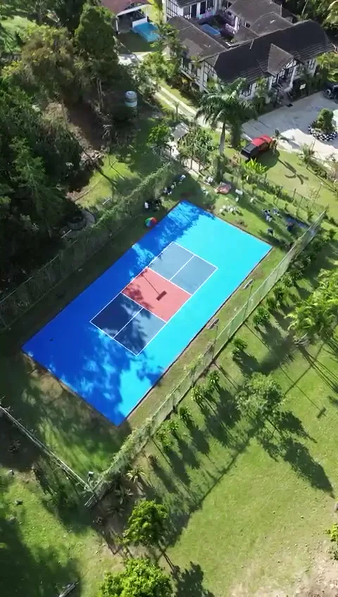 Aerial view of the blue pickleball court with the Tudor Bungalow beyond